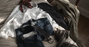 Fyra basplagg, vit skjorta, jeans, kavaj och kängor, upplagda tillsammans på en säng